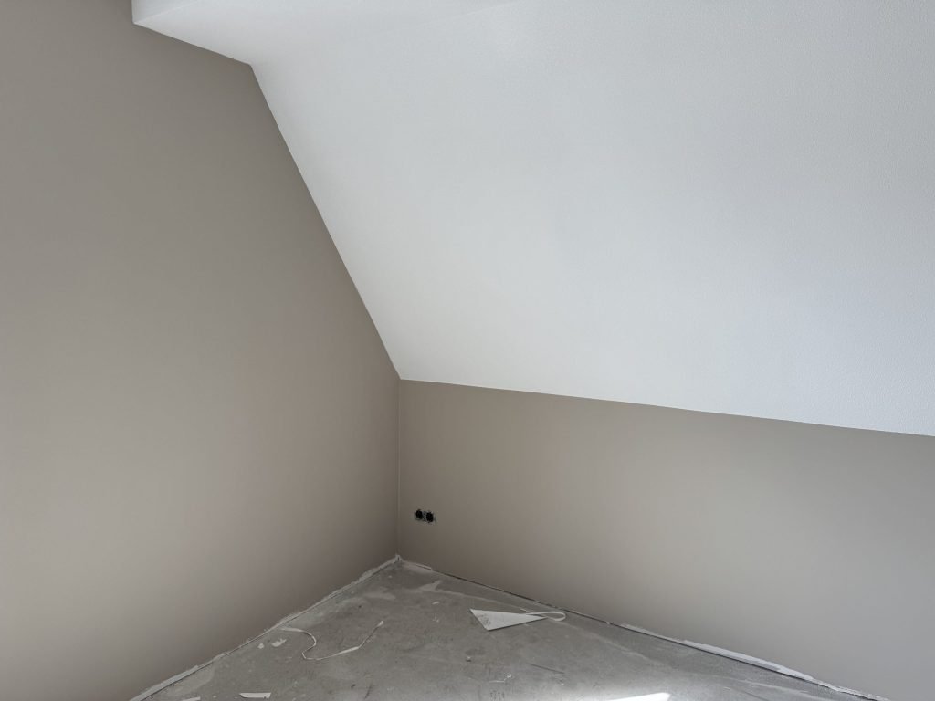 Zolderkamer in een nieuwbouwhuis met strak afgewerkte wanden onder de schuine kap