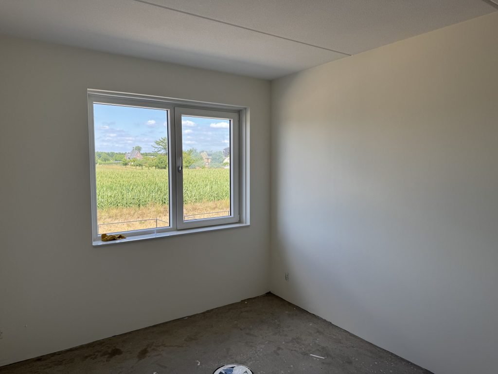 Lege nieuwbouwkamer met gladde lichte wanden en een groot raam, kort na de oplevering