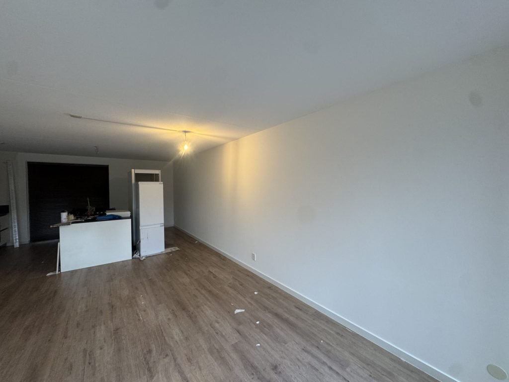 Lange witte wand in een woonkamer met open keuken, klaar na het behangen en sauzen